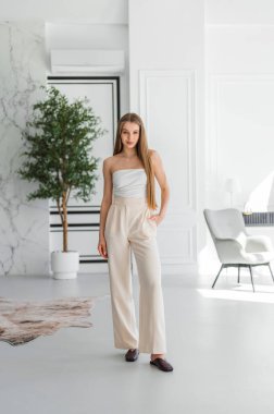 Modaya uygun genç bir kadın şık, modern bir dairede poz veriyor, açık renkli giyiniyor, kendine güveni ve tarzı var..