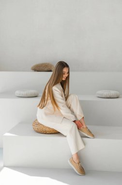 Bir model şık bej bir kıyafet sergiliyor, minimalist bir yüzeyde zarifçe oturuyor. Modern moda çekimleri için mükemmel..
