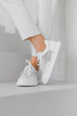 Gösterişli, modern bir ortamda açık renk pantolonla eşleştirilmiş şık beyaz spor ayakkabıları şık ve gündelik bir ayakkabı seçimi sergiliyor..