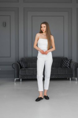 Şık genç bir kadın minimalist bir mekanda duruyor, moda içeriği için mükemmel, zarif ve kendine güvenen bir kıyafet sergiliyor..