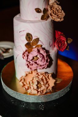 Gelin ve damat düğün ziyafetinde köy pastalarını kesiyorlar. Eller zarif pembe çiçeklerle pastayı keser..