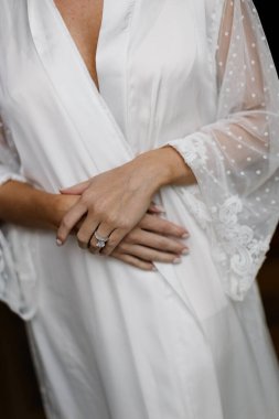Zarif bir nişan yüzüğü ve alyans içeren, zarif dantel bir bornozla güzelce tasarlanmış bir gelin eli. Düğün hazırlığının ebedi ve romantik bir ayrıntısı..
