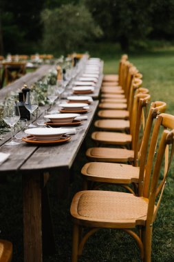 Güzel bir açık hava düğün resepsiyonu, uzun ahşap masalar, sarı sandalyeler, ve kırsal Toskana şatosu ortamında telli ışıklar. Zeytin ağaçları ve tarihi mimari ile çevrelenmiş bu görüntü, zamanın zarafetini ve cazibesini yakalar. 