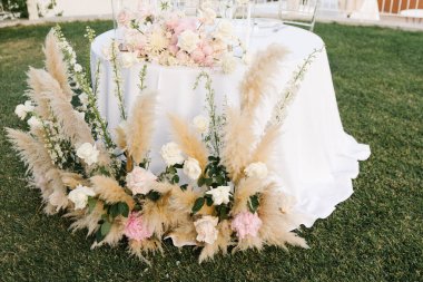 A stunning wedding table set against a picturesque countryside backdrop. The arrangement features pampas grass, white and blush roses. clipart