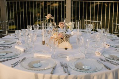 Göz kamaştırıcı bir düğün masası. Resimli bir kırsal alana kurulmuş. Düzenlemede pampalar çimenler, beyaz ve allık güller yer alıyor.