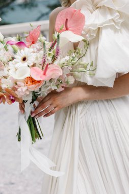 Tropikal anturyumlar, hassas orkideler, papatyalar ve bahçe güllerinin karışımından oluşan canlı bir gelin buketi..