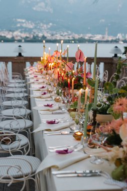 Parlak mumlarla, canlı çiçeklerle ve zarif sofra eşyalarıyla süslenmiş büyüleyici bir akşam sofrası. Atmosfer romantik ve sofistike, pastel çiçekler, inciler ve