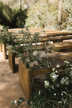 Sakin bir orman ortamında güzel bir açık hava düğün töreni düzenlendi. Ahşap banklar koridor boyunca uzanır, yemyeşil çiçeklerle süslenir ve zarif çiçeklerle süslenir.