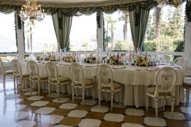 Güzel dekore edilmiş bir düğün masası zarif bir mekanda, manzaralı bir göl ve palmiye ağaçlarına bakan büyük pencereli..