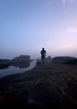 Adam gün doğumunda sisli bir kayalık nehir boyunca koşar. 3 Boyutlu Hazırlama.