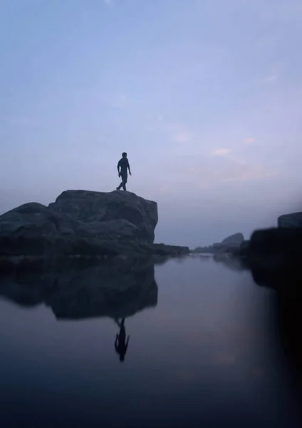 日出时 人在雾蒙蒙的湖畔的岩石上行走 3D渲染 — 图库照片