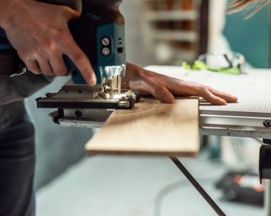 Adam testere masasındaki tahta rafı testereyle kesiyor..