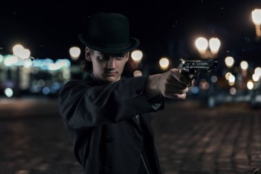 Gece vakti sokakta şapkası ve paltosu olan genç bir Victoria 'lı silah doğrultuyor..