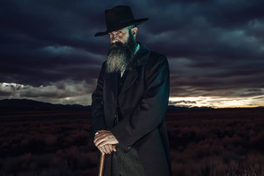 Şapkalı ve paltolu klasik Viktoryalı adam alacakaranlıkta bastonuyla dikiliyor..