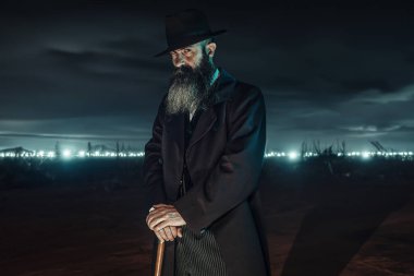 Şapkalı ve paltolu klasik Viktoryalı adam alacakaranlıkta bastonuyla dikiliyor..