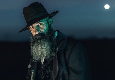 Şafak vakti manzarada duran şapkalı ve paltolu muhafazakar adam..