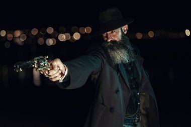 Viktorya döneminden kalma, şapkalı ve paltolu bir adam geceleri dışarıda tabancayla ateş ediyor..