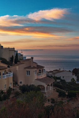 Gün batımında yeşil bitki örtüsü olan bir tepenin yamacındaki İspanyol kıyı yerleşim bölgesi..