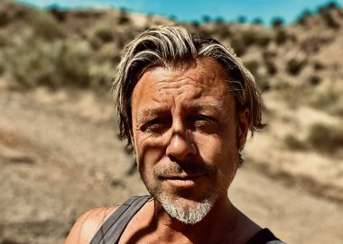 Bronz tenli, sakallı, atlet gömlekli, güneşli bir ortamda sarışın bir adam..