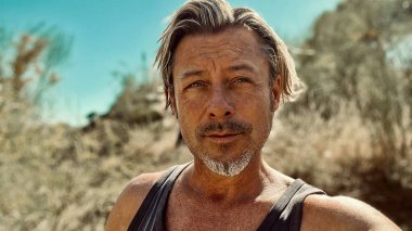 Bronz tenli, sakallı, atlet gömlekli, güneşli bir ortamda sarışın bir adam..