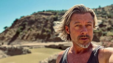 Güneşli ve rüzgarlı bir ortamda atlet tişörtlü, esmer, sarışın bir adam..