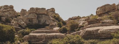 Mavi gökyüzünün altındaki yeşil bitki örtüsü arasındaki kireçtaşı kaya oluşumları. El Torcal de Antequera Ulusal Parkı. Endülüs. İspanya.