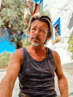 Bronzlaşmış sarışın bir adamın şişmiş yüzü gri sakallı, beyaz bir İspanyol evinin önünde oturuyor. Eşek arısı soktu..