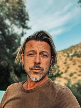 Bronz tenli, yarı sarı saçlı ve kahverengi tişörtlü gri sakallı adam İspanya 'da güneşli yaz havasının tadını çıkarıyor..