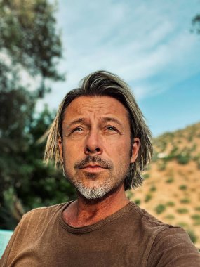 Bronz tenli, yarı sarı saçlı ve kahverengi tişörtlü gri sakallı adam İspanya 'da güneşli yaz havasının tadını çıkarıyor..