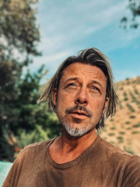 Bronz tenli, yarı sarı saçlı ve kahverengi tişörtlü gri sakallı adam İspanya 'da güneşli yaz havasının tadını çıkarıyor..