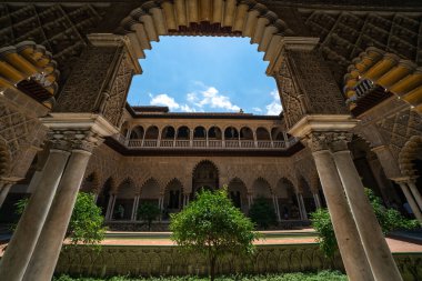 Explore a breathtaking view through the archway of Sevilles Alczar, showcasing intricate architecture and vibrant greenery. clipart