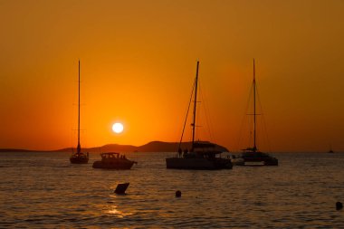 Ibiza 'daki canlı turuncu gökyüzüne karşı yelkenli silueti ile denizin üzerinde sersemletici bir gün batımı..