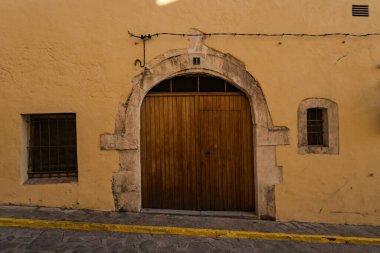İspanya 'da canlı sarı bir duvar tarafından çerçevelenmiş, geleneksel mimarinin özünü yansıtan kırsal ahşap bir kapı manzarası..