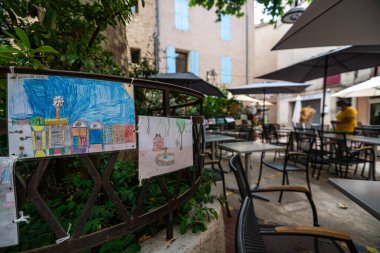 Explore a beautiful caf in Menasque, Provence, featuring delightful childrens drawings. A perfect depiction of local culture and community spirit. clipart