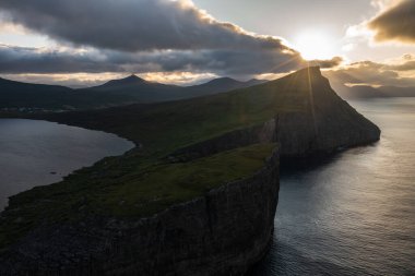 Gün batımında Faroe Adaları 'nın engebeli uçurumlarını ve sakin sularını yakalayan çarpıcı bir dron atışı. Seyahat meraklıları için mükemmel bir manzara..