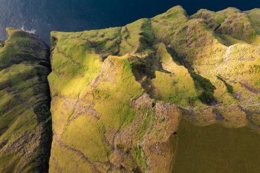 Faroe Adaları 'ndaki okyanusa bakan canlı yeşil uçurumların insansız hava aracı görüntüsü. Doğa ve seyahat projeleri için mükemmel..