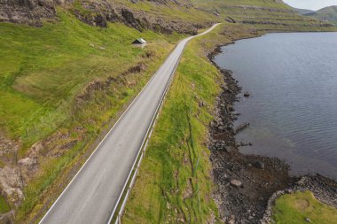 Faroe Adaları 'nın kayalıkları boyunca uzanan ve yemyeşil ve sakin suları gözler önüne seren dolambaçlı bir yolun çarpıcı görüntüsü..