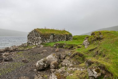 Faroe Adaları 'ndaki sakin suların yanındaki eski taş kalıntılarının huzur veren güzelliğini keşfedin. Doğanın ve tarihin özünü yakalayın..
