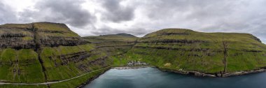 Yazın sonunda Faroe Adaları kıyısındaki yemyeşil kayalıkların ve köyün nefes kesici hava manzarası..
