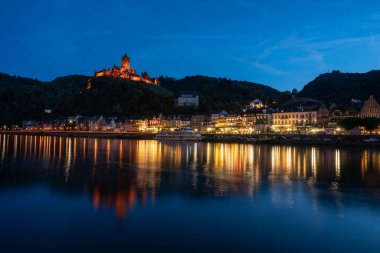 Cochem Kalesi 'nde baş döndürücü bir yaz alacakaranlığı, Moselle Nehri' nin parlak yansımaları. Seyahat meraklıları için resim gibi bir manzara.
