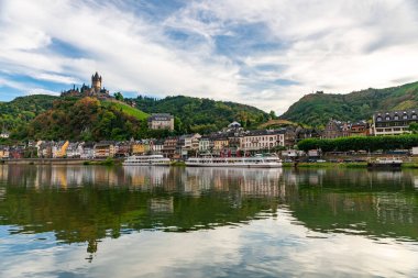 Cochem Kalesi yakınlarındaki resimli yaz manzarasını keşfedin. Canlı binaları ve Moselle Nehri boyunca uzanan verimli tepeleri yansıtın..