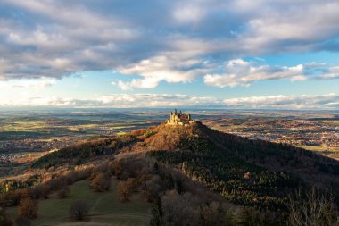 Hohenzollern Kalesi 'nin bulunduğu göz kamaştırıcı sonbahar manzarası, canlı yeşillikler ve dramatik bulutlarla çevrili bir tepede..