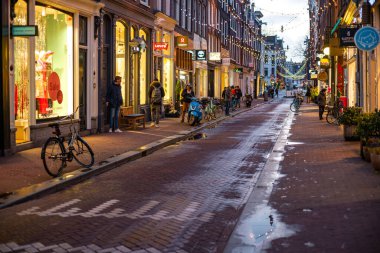 Amsterdam 'daki antika bir caddenin büyüleyici akşam manzarası, vitrinler, bisikletler ve ıslak kaldırımlara yansıyan şenlikli ışıklar..