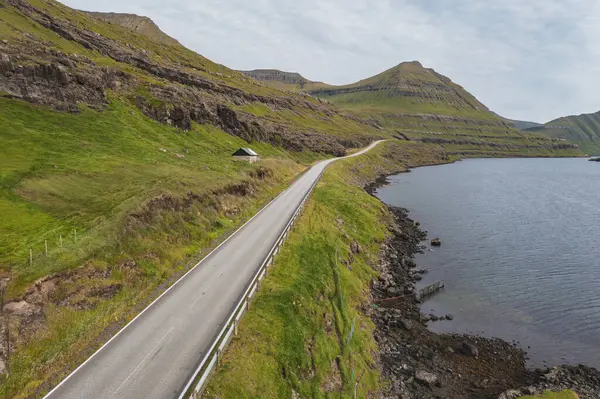Faroe Adaları 'ndaki dolambaçlı kıyı yolunun nefes kesen manzarası dramatik manzaralar ve sakin sular sergiliyor..