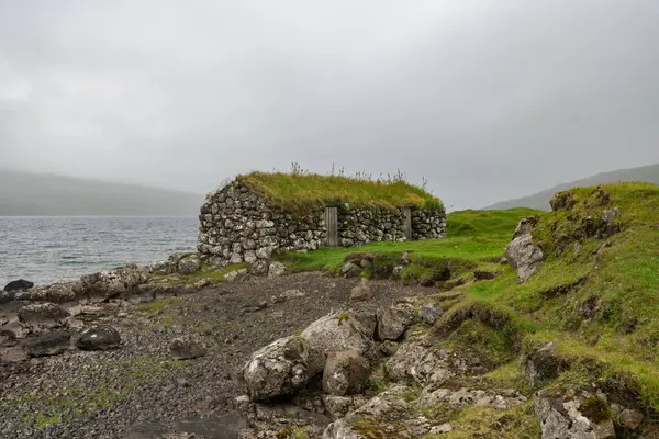 Çimenli çatılı, huzurlu bir taş yapı. Yaz sonlarında sisli, Faroe Adaları 'nın sakin kıyıları tarafından yuva yapmış..
