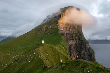Gün batımında Faroe Adaları 'nın çarpıcı hava manzarası, dramatik uçurumlar ve deniz feneri. Seyahat ve doğa temaları için mükemmel..