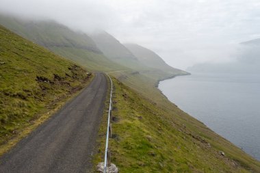 Faroe Adaları 'nın sakin kıyı şeridi boyunca uzanan ve bereketli manzaralarını ve sisli dağlarını gözler önüne seren çarpıcı bir dron görüntüsü..