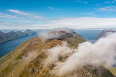 Faroe Adaları 'nın engebeli güzelliğini gösteren, sis ve güneş ışığıyla örtülü, nefes kesici drone çekimi..