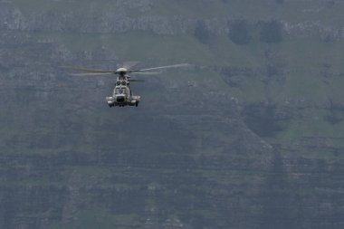 Faroe Adaları 'nın nefes kesici uçurumlarının üzerinde süzülen çarpıcı bir askeri helikopter güzellikleri ve havacılık becerilerini sergiliyor..