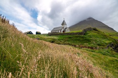 Faroe Adaları 'ndaki yemyeşil yemyeşil bir alana kurulmuş dingin bir kilisenin nefes kesici hava manzarası büyüleyici yaz manzaralarını gözler önüne seriyor..